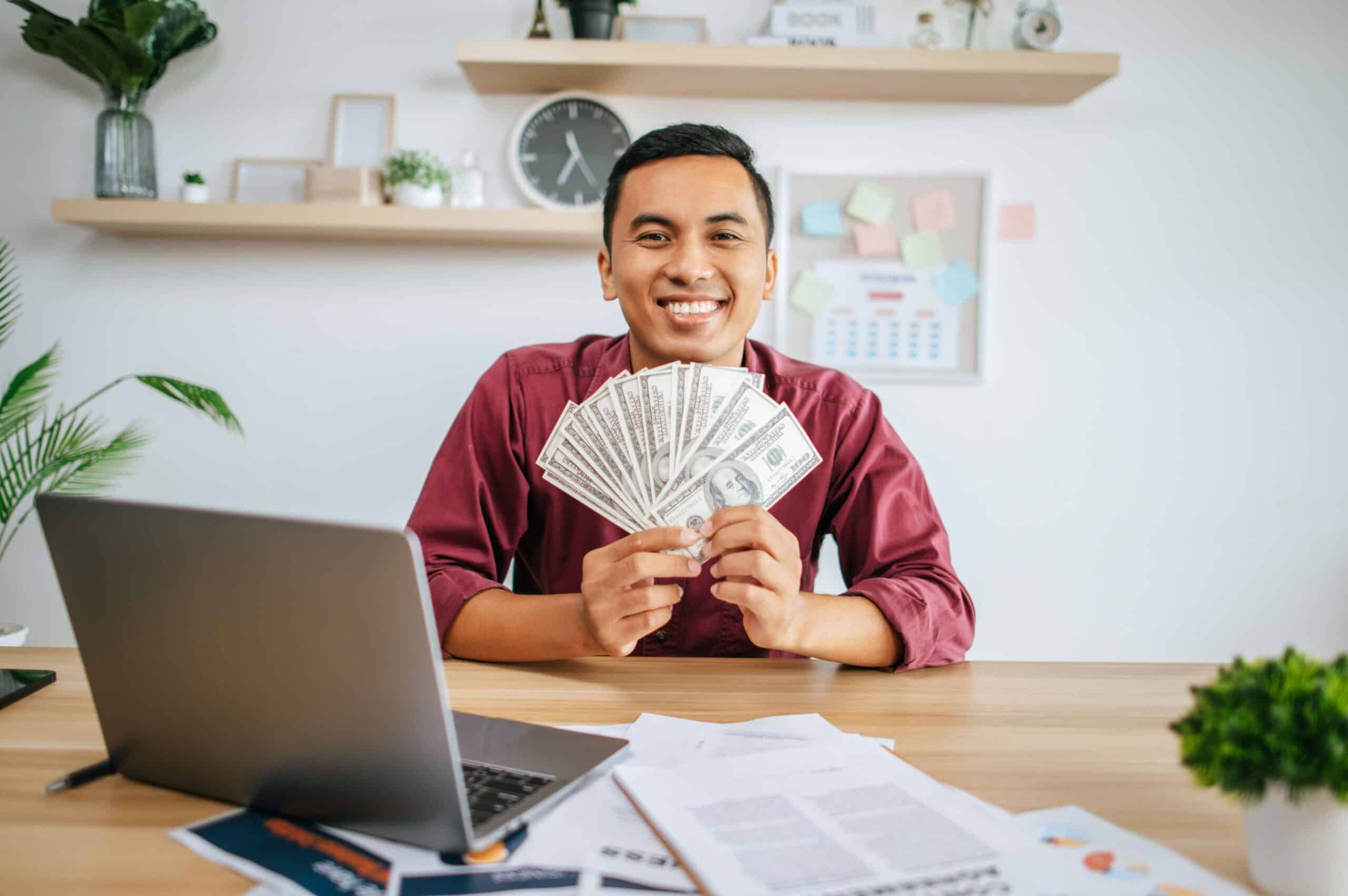 man-working-office-holding-money-with-laptop-documents-desk (1) Express Loans in Manitoba<br />